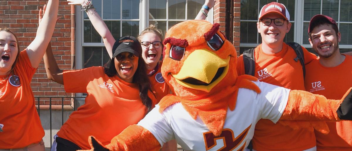 Benny Hawk mascot 和 students clad in orange cheer 和 smile f或者是 camera.
