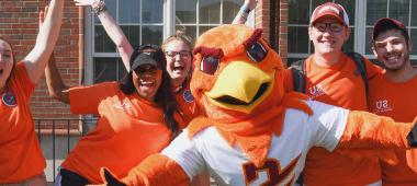本尼·霍克吉祥物和学生们穿着橙色的衣服对着镜头欢呼和微笑.
